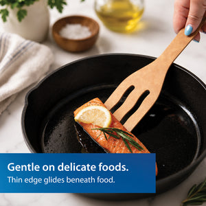 The Everyday Slotted Turned from Rada is shown lifting salmon from a black cast iron skillet on a white marble countertop. A blue text banner at the bottom reads, 'Gentle on delicate foods. Thin edge glides beneath food.'