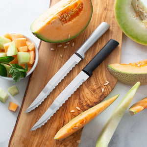 Two serrated knives on a wooden cutting board with sliced melons and a bowl of melon pieces.