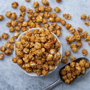 Caramel popcorn in a bowl spread out with a popcorn scooper.