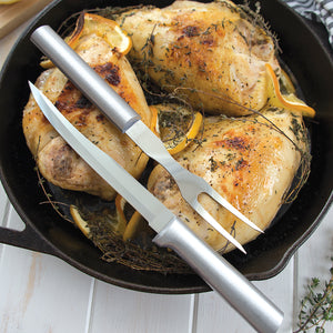 Carver/Boner Knife and Carving Fork with silver handles on chicken pieces in cast iron pan.