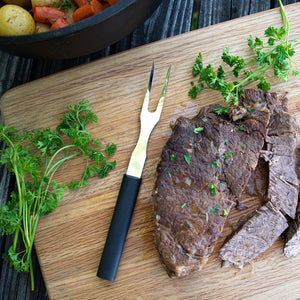 Black handle Carving Fork on a cutting board with a roast, greenery, carrots, potatoes, and more.