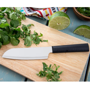 Cook's Utility knife with black handle on wooden cutting board with herbs.