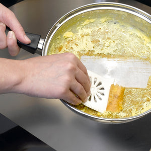 A cook using the Rada Daisy PanMate Scraper to scrape off baked-on scrambled eggs out of a frying pan.