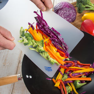 Broccoli, peppers, and cabbage sliding off flexible plastic cutting board into wok.