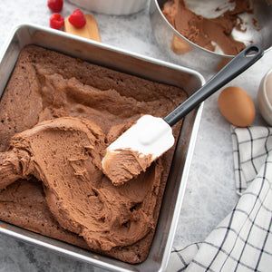 Spreading chocolate frosting over a pan of chocolate brownies.