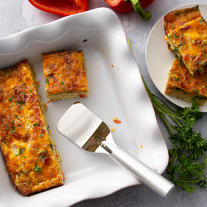 Rada's silver Mini Server handle in a white pan with sliced egg bake around it as well as greenery and cut pepper.