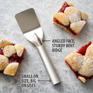 Serving spatula on a marble counter with squares of Cherry bars. Angled face, sturdy bent ridge. Small on size, big on uses.