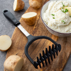 Potato Masher laying on cutting board, bowl of mashed potatoes with garnish, and whole potatoes.