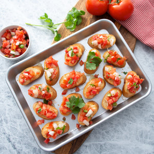 Quarter Sheet Pan filled with bruschetta on cutting board with tomatoes and basil.