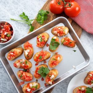 Toasted bread topped with chopped tomatoes on a Quarter Sheet Pan with red checked napkin.