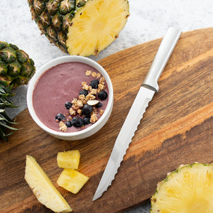 A bowl of fruit yogurt topped with granola, blueberries and sliced almonds. Using the serrated slicer to slice pineapple.