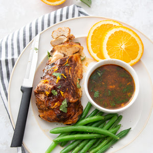 The black handled Rada serrated steak knife slicing barbequed chicken with a cilantro dipping sauce and a lemon garnish.