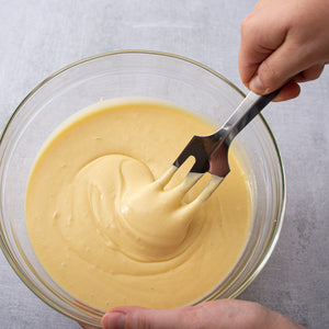 Rada's Serverspoon lifted out of a bowl of yellow cake batter, halfway in the bowl.