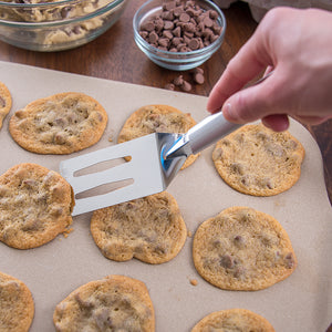Spatula with silver handle removing chocolate chip cookies from baking stone.