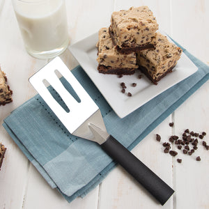 Spatula with black handle on blue napkin by chocolate chip bars stacked on plate.
