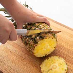 Silver handle slicing a pineapple on a cutting board.