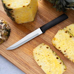 Black handle Stubby Butcher laying on a cutting board next to a pineapple with the sides cut off.