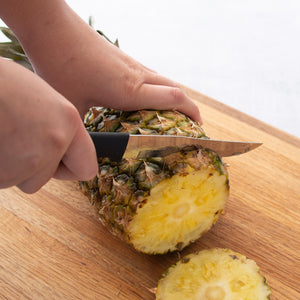 Black handle slicing a pineapple on a cutting board.