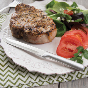 Utility/Steak Knife with silver handle on plate with meat, spinach and tomatoes.