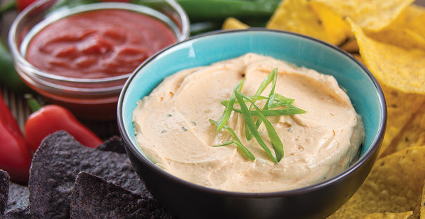 A savory bowl of RADA's Sriracha Ranch Dip Quick mix with some garnish on top next to a red chilies and a bowl of salsa