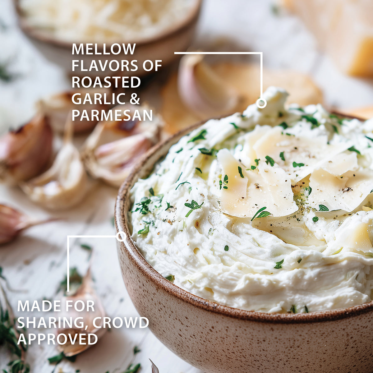 A close-up of the Roasted Garlic and Parmesan Dip in a speckled brown ceramic bowl, garnished with fresh parsley and shaved cheese. Blurred garlic cloves and herbs sit in the background.