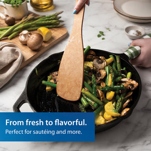 Rada's wooden Heavy-Duty Saute Spoon used for sauteing vegetables in a black cast iron skillet. A hand holds the handle, and a ble text banner at the bottom reads 'From fresh to flavorful.'