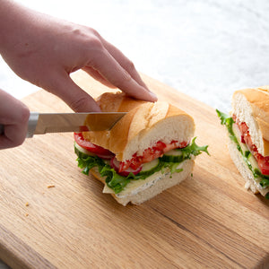 8" Bread Knife slicing through loaded sandwich on a brown cutting board.