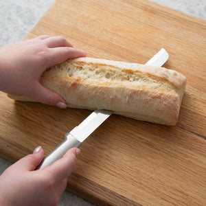 Rada Cutlery silver handle 8" Bread Knife slicing a baguette horizontally on a cutting board.