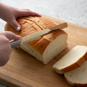 Silver handle Bread Knife cutting a loaf of bread on a board into slices.