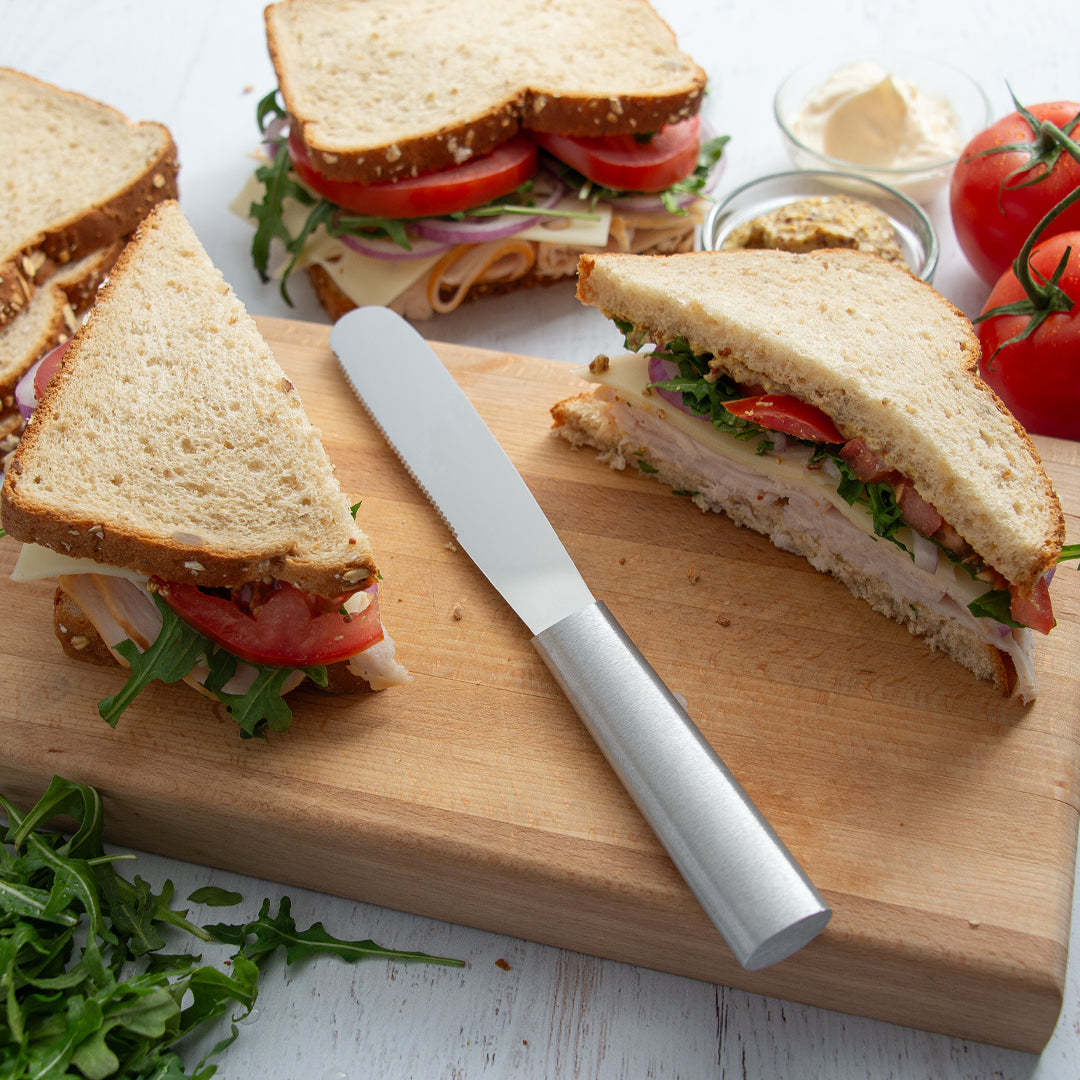 Sandwiches on a wooden cutting board with a knife, surrounded by fresh ingredients.
