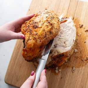 Person cutting a roasted chicken breast on a wooden cutting board.