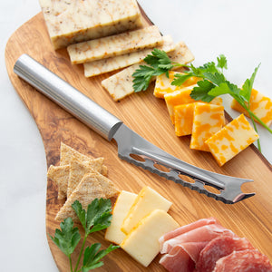 Wooden cutting board with sliced cheese, herbs, and a cheese knife on a white background