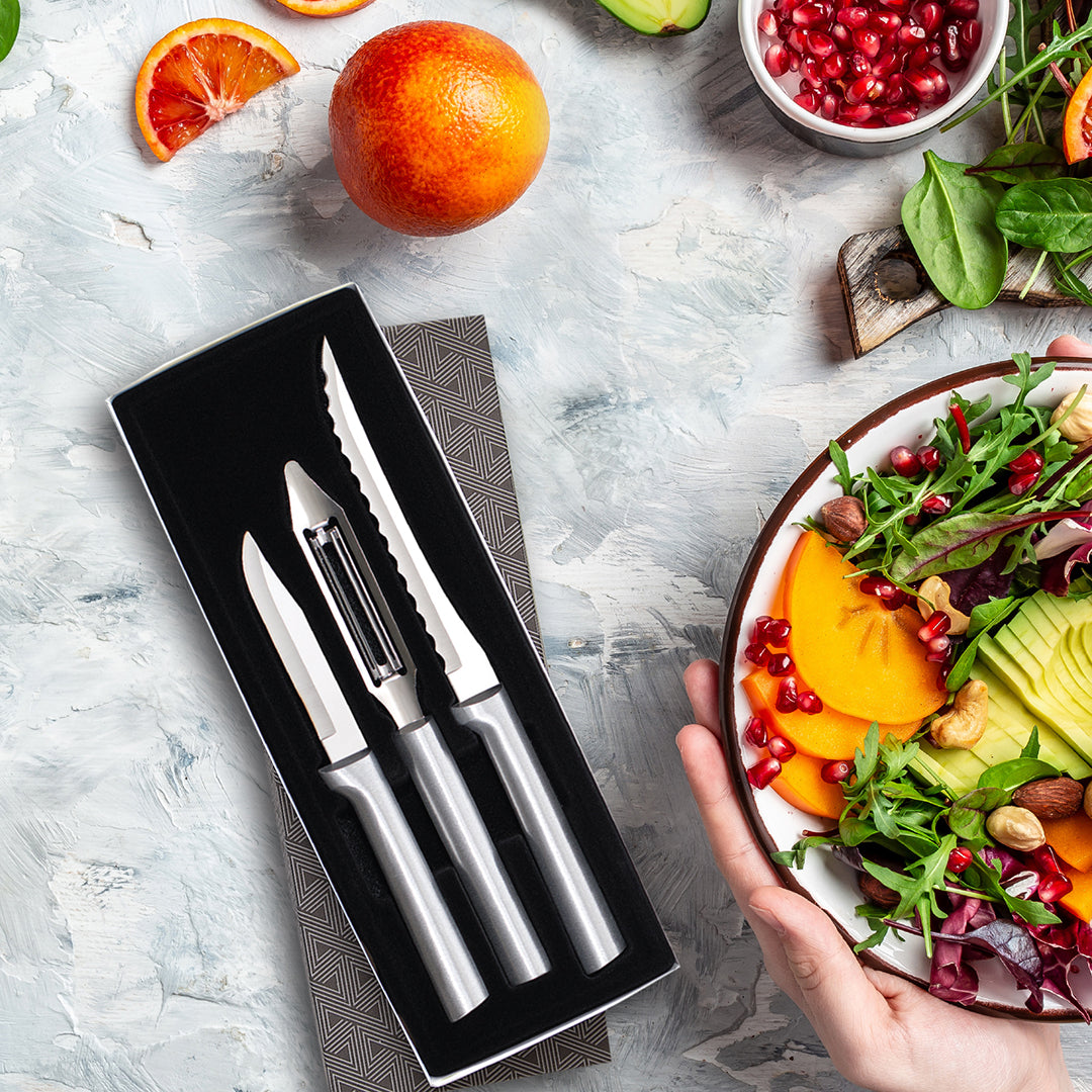 Set of kitchen knives in a box with a salad and fruits on a table