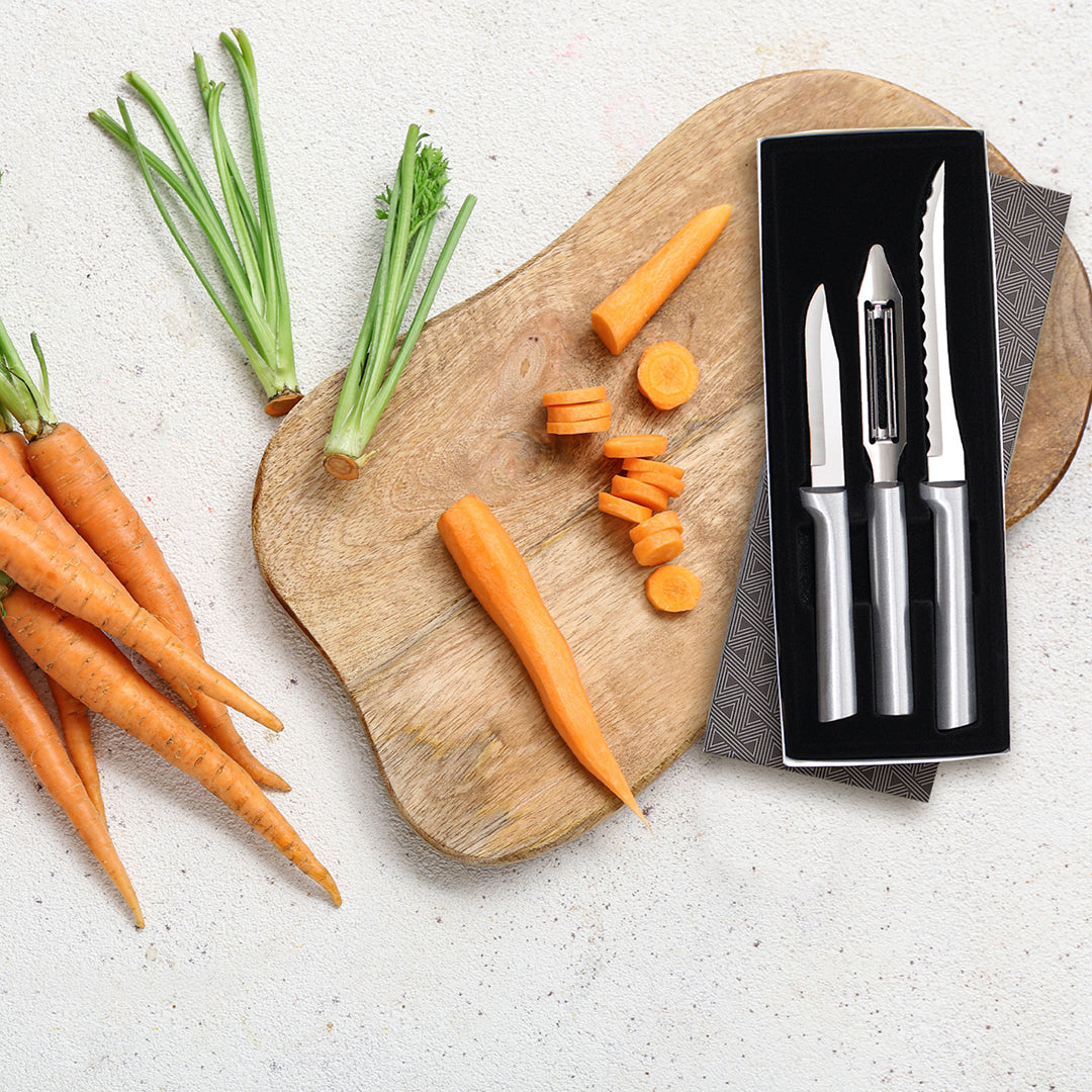 Carrots on a wooden cutting board with a set of knives in a black sheath.