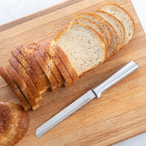 Rada's silver handle Bread Knife laying on a cutting board with a sliced loaf of bread.