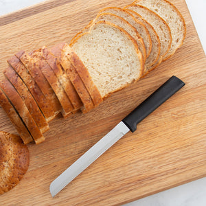 Rada's black handle Bread Knife laying on a cutting board with a sliced loaf of bread.