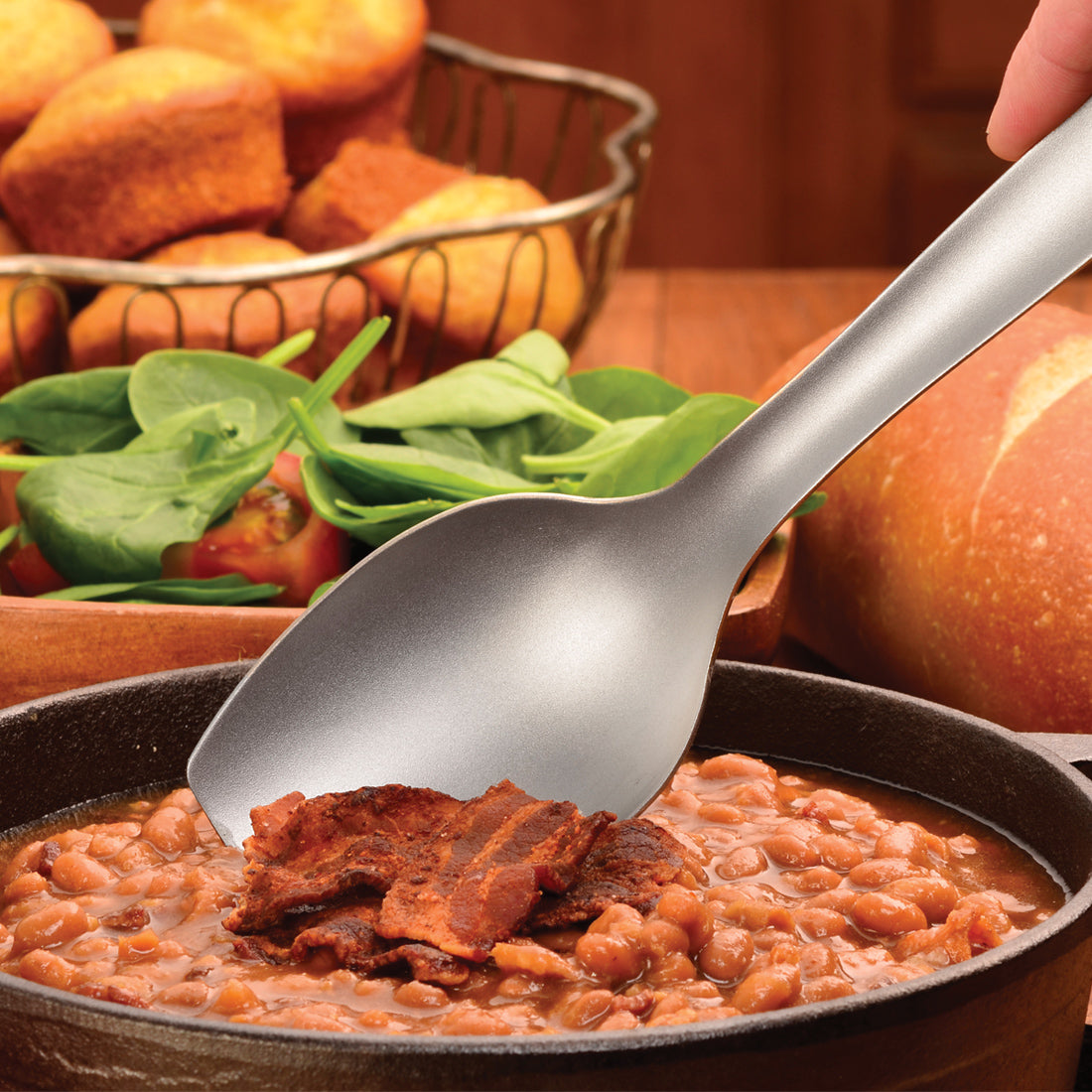 Cook's Spoon scooping a portion of baked beans with a bacon topping