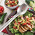 Cook's Spoon w/Holes on top of a sliced chicken salad with lettuce, tomatoes, and cucumber