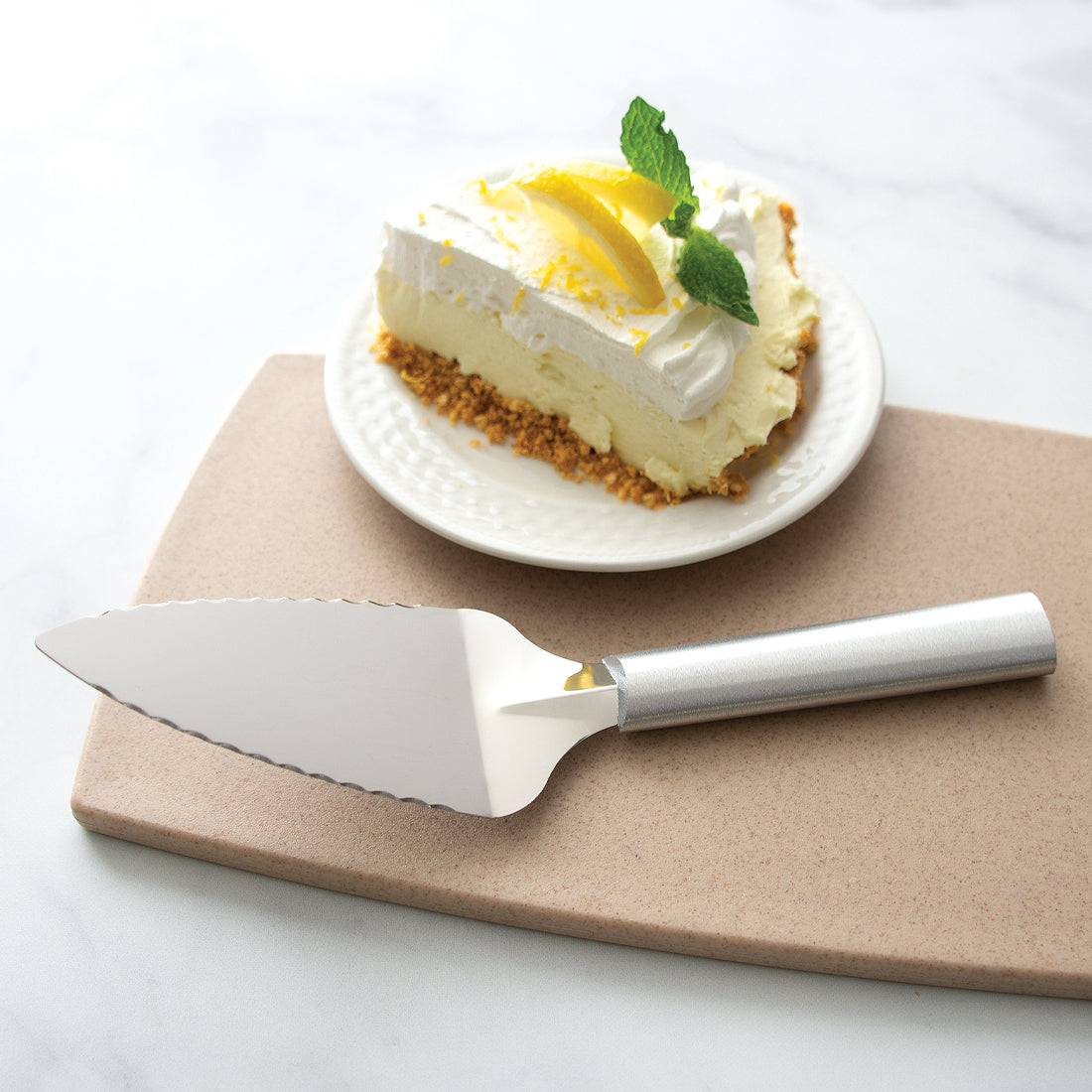 Rada Cutlery Serrated Pie Server with silver handle and slice of lemon cheesecake on white plate. 