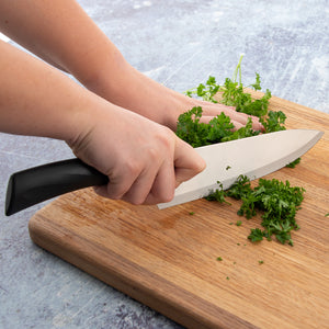 Anthem Wave French Chef Knife in use mincing herbs on a wooden cutting board