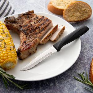 Anthem Wave Serrated Steak knife on white plate with sliced pork chop and sweet corn 