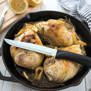 Non-serrated Anthem Wave Slicer knife with chicken in cast iron pan garnished with citrus