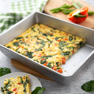 Serving up a cake pan of baked omelet with spinach, tomato and feta.