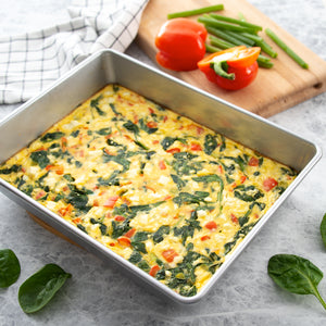 Egg bake with tomato, feta and spinach in a cake pan with a cutting board, bell pepper, and spinach.