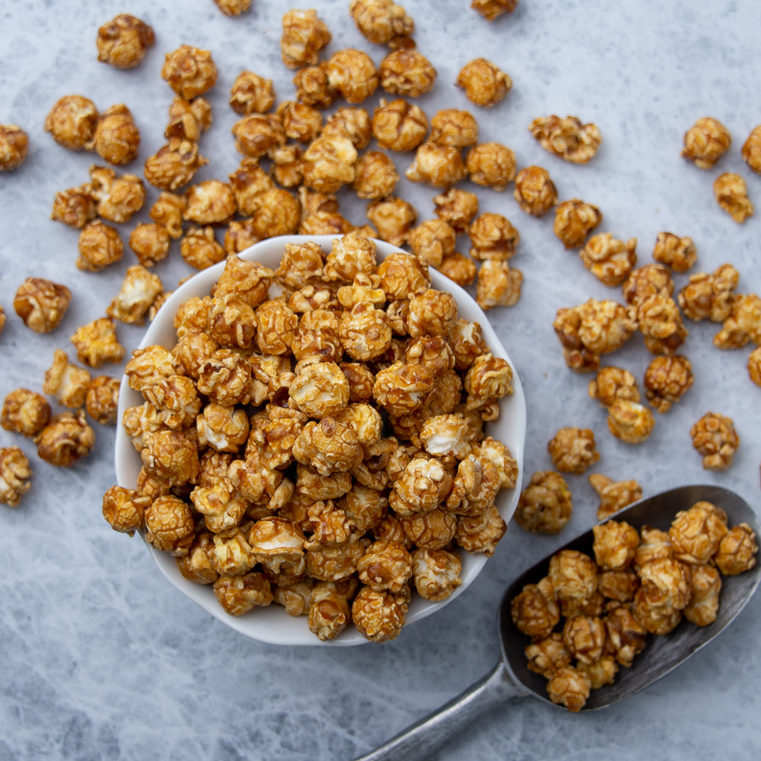 Caramel popcorn in a bowl spread out with a popcorn scooper.