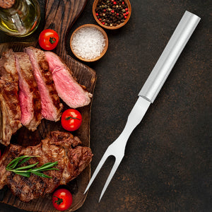 Rada's silver handle Carving Fork laying next to a cutting board with a grilled steak, tomatoes, and seasonings on top of it.