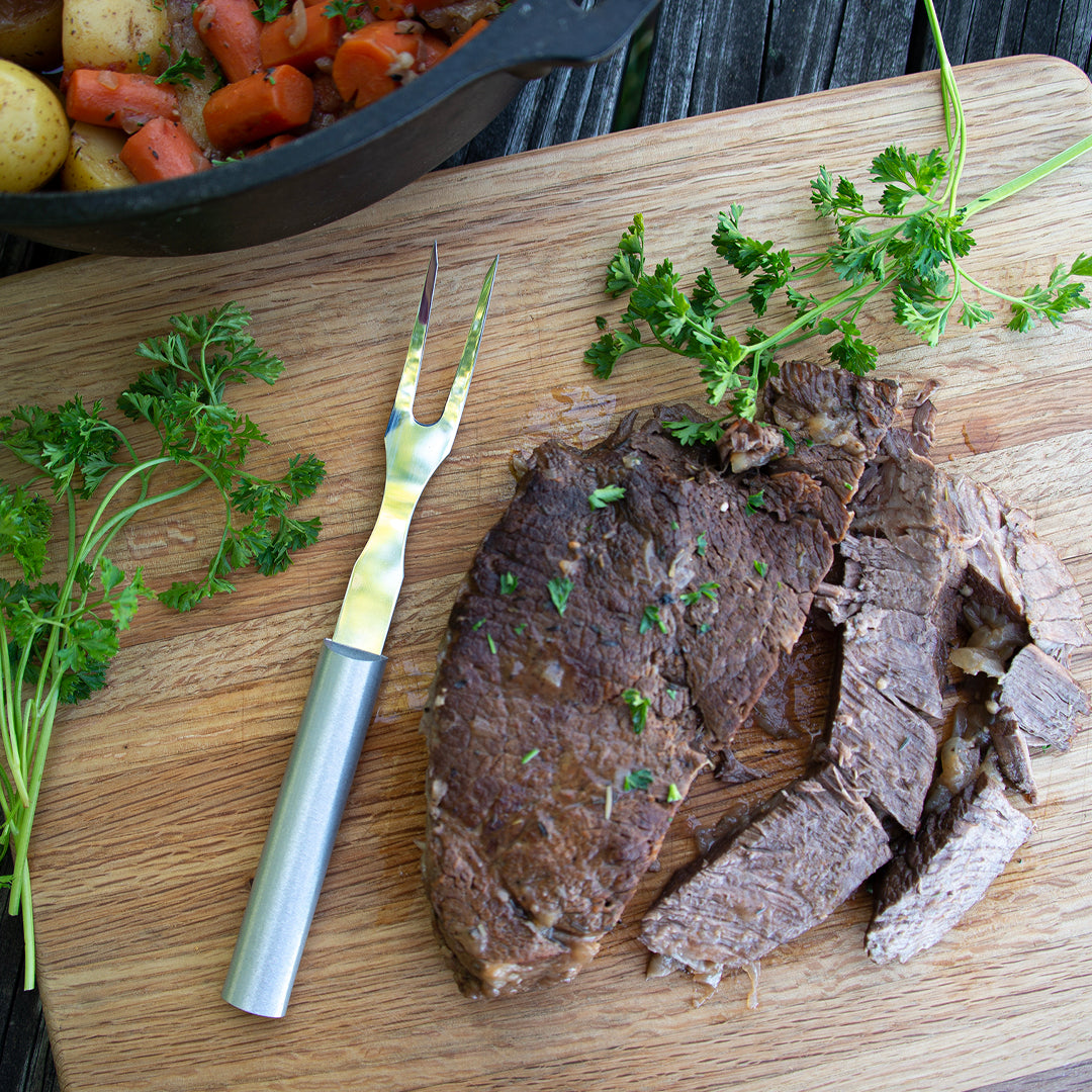 Silver handle Carving Fork on a cutting board with a roast, greenery, carrots, potatoes, and more.
