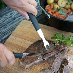 Rada Cutlery Carving Fork and knife slicing a roast on a cutting board with potatoes and carrots in the background.