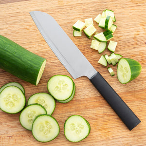 Black handle Cook's Knife next to a whole, chopped, and diced cucumber laying on a cutting board.