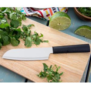 Cook's Utility knife with black handle on wooden cutting board with herbs. 